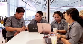 Four McDonald’s employees smiling, sitting around a table with laptops